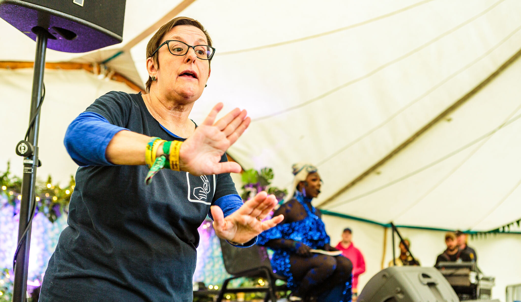 a lady is in the foreground mid sign-language as she is translating for a performer on the stage in the background.