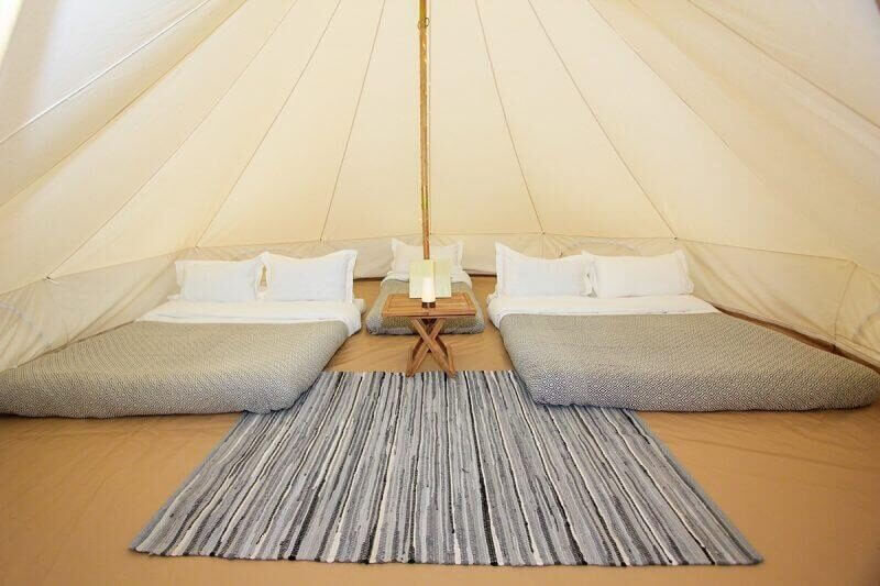 2 double mattress with bedding separated by a single mattress with bedding and pop up table with a rug at the entrance of the tent