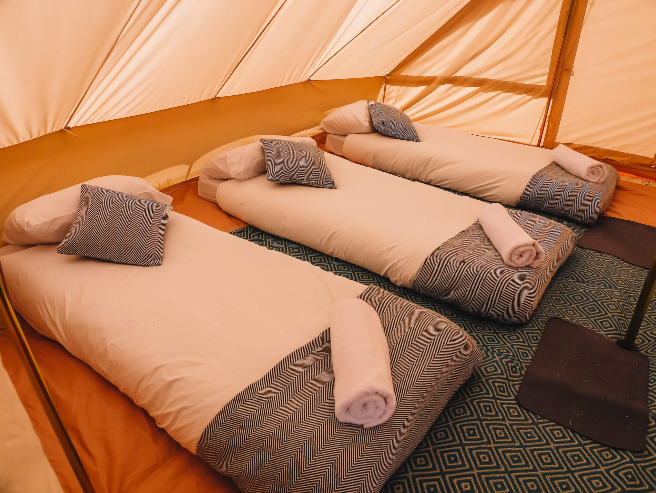 3 single mattresses with bedding and a rolled up towel on the end of the bed